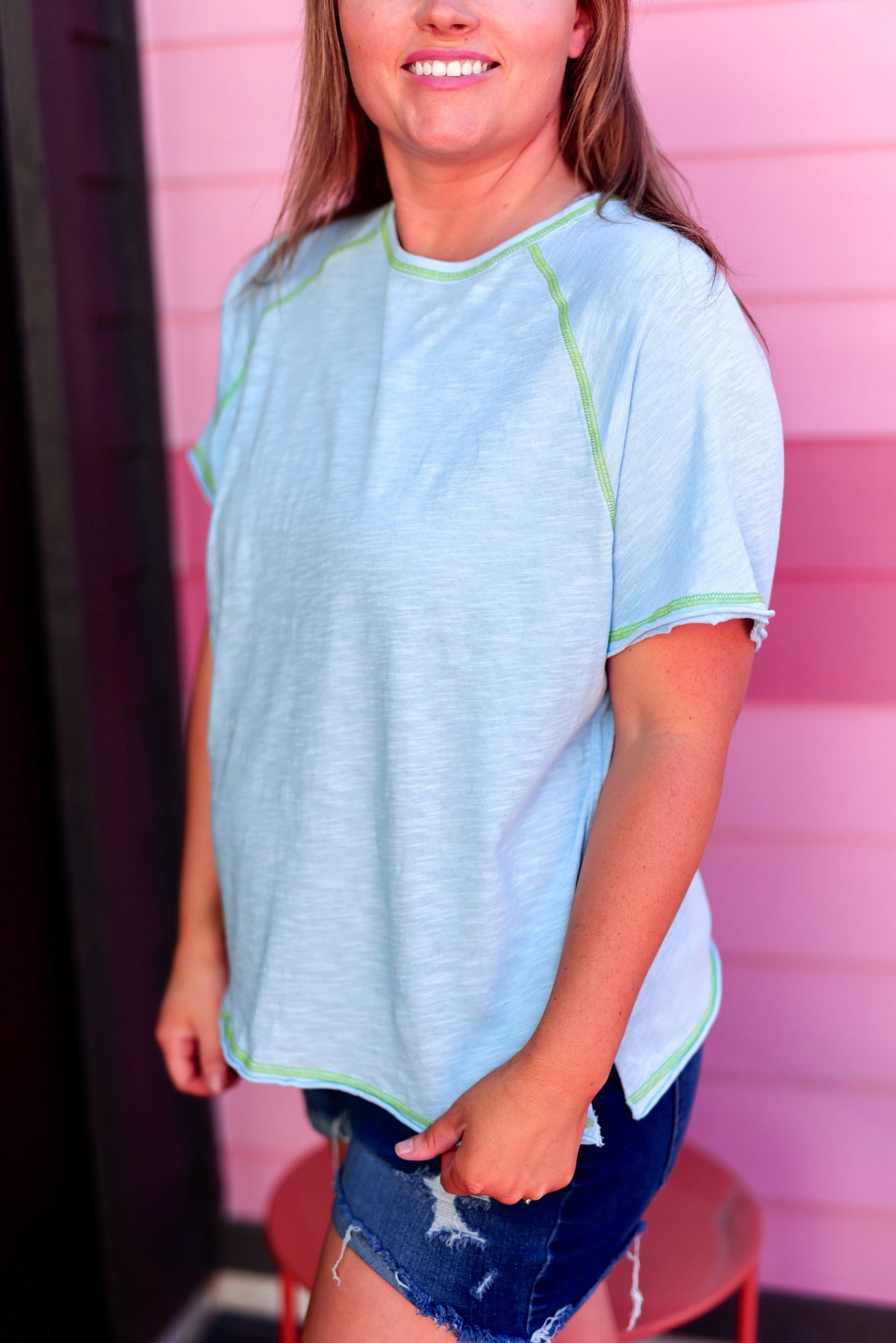 Light blue short-sleeve women's top with green stitching and a relaxed fit, perfect for casual outings.