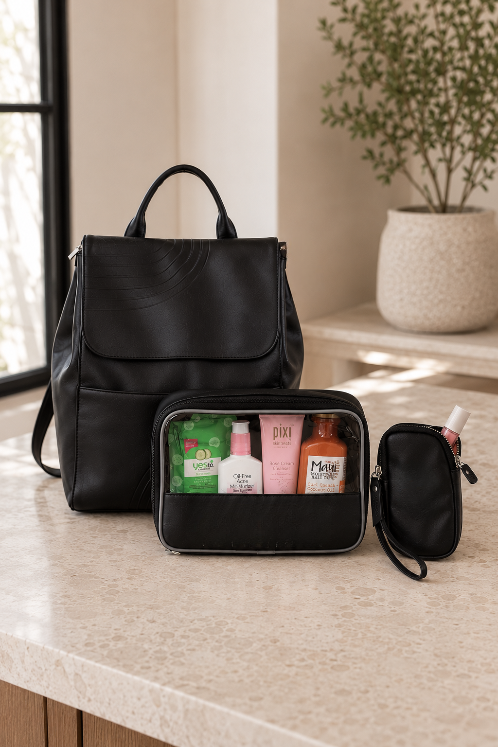 A black leather-like backpack sits on a beige stone countertop beside a matching black toiletry bag filled with assorted bottles and a small zip pouch, with a softly blurred indoor background and potted plant.