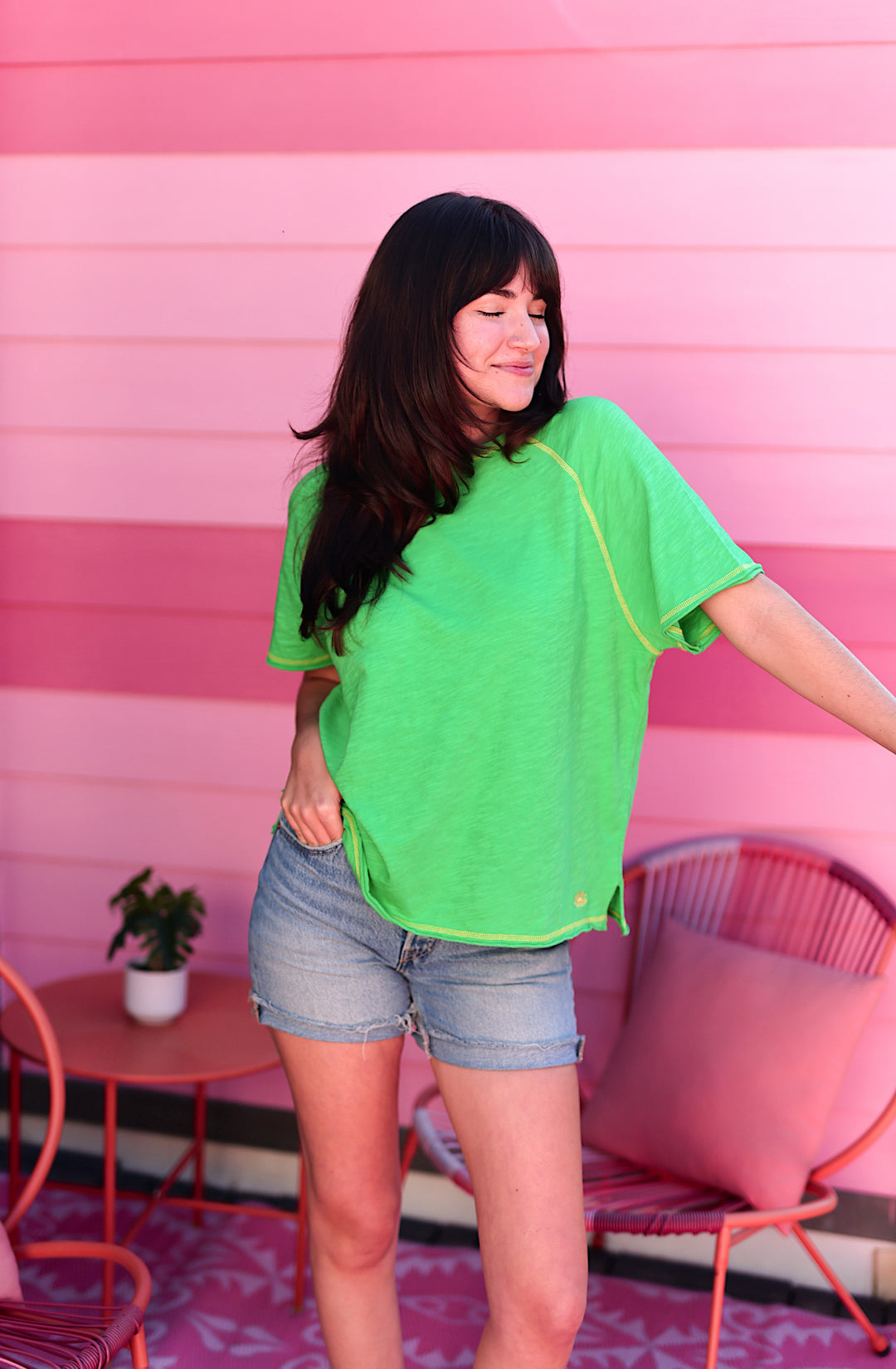 Woman wearing a bright green raglan tee with contrast stitching and denim shorts.