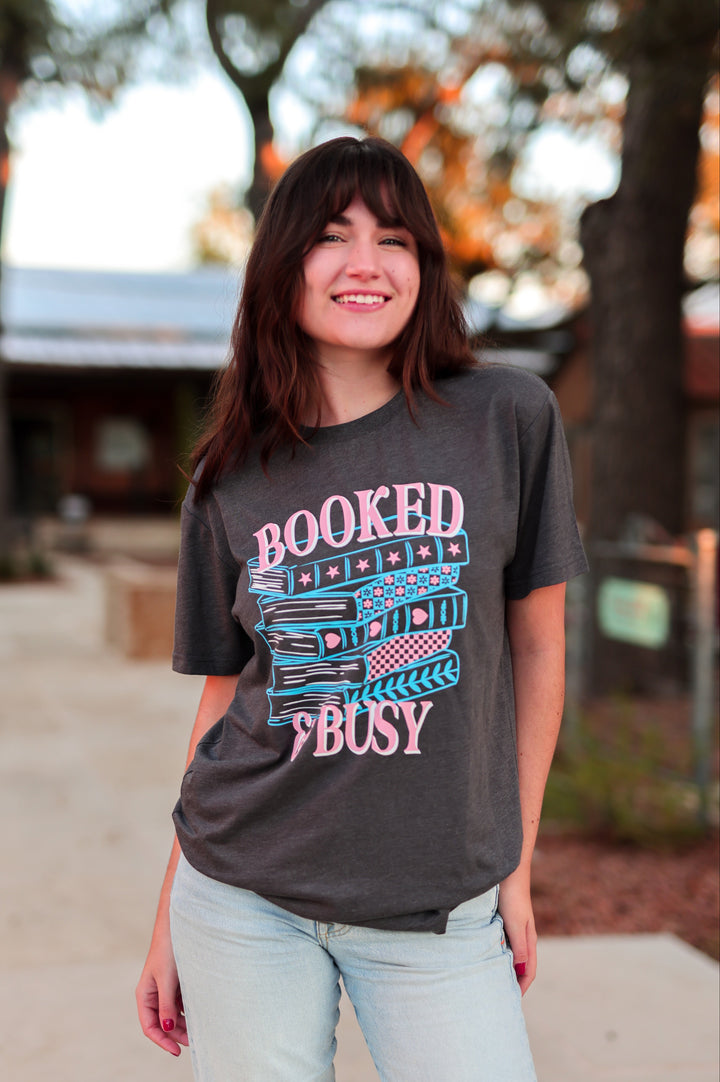 Woman wearing a 'Booked & Busy' t-shirt outdoors