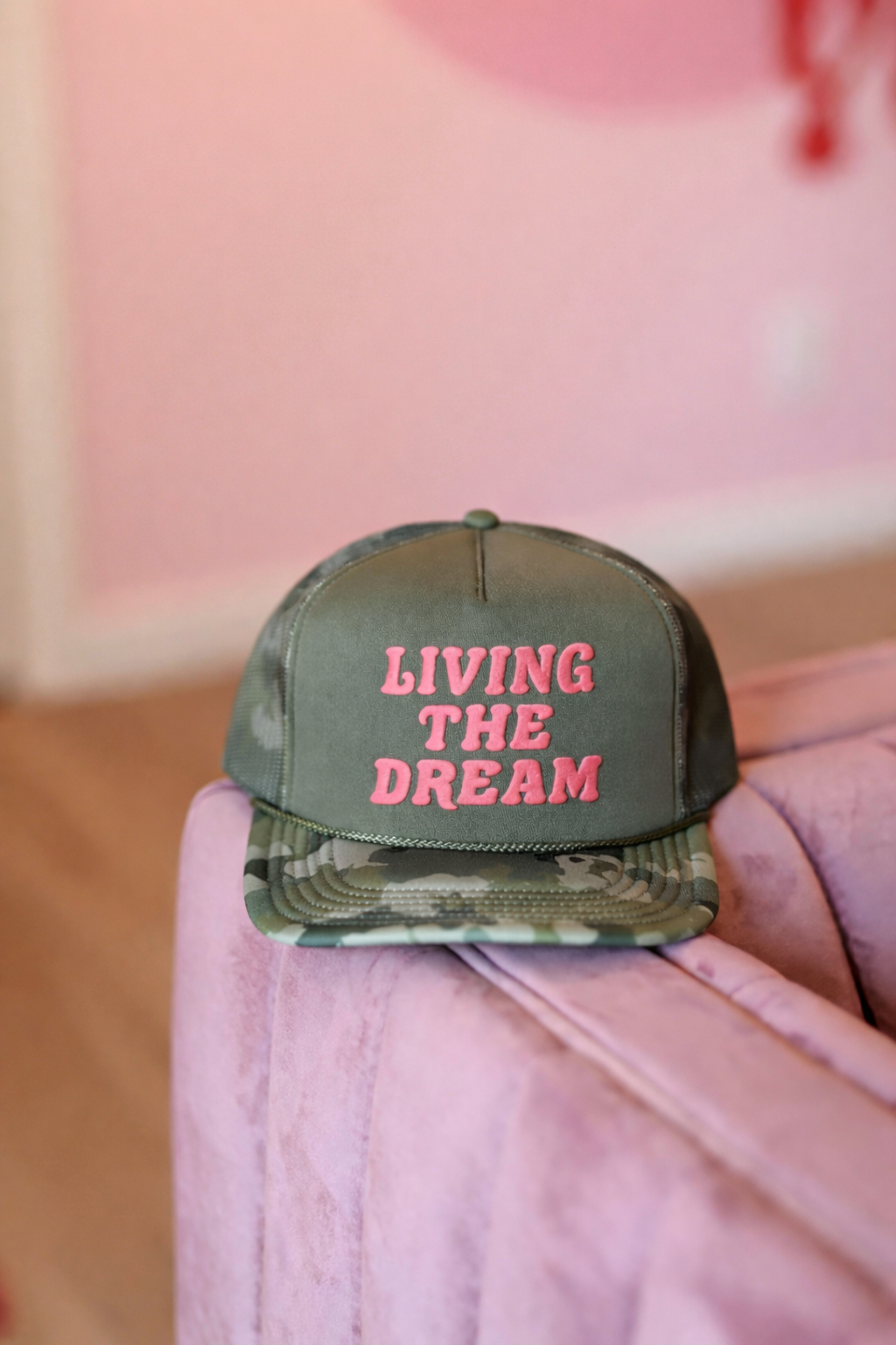 Green camouflage cap with 'Living the Dream' text on a pink surface