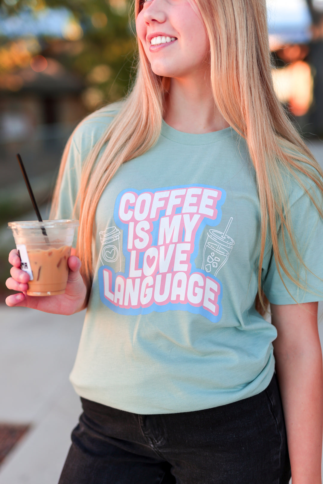 Person wearing a t-shirt with 'Coffee is my love language' text, holding a coffee cup.