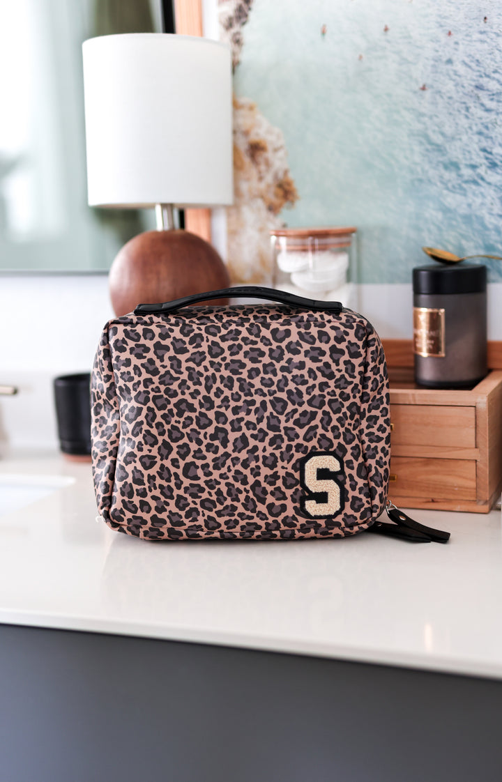Leopard print pouch with a letter 'S' on a surface with a lamp and decor items in the background.