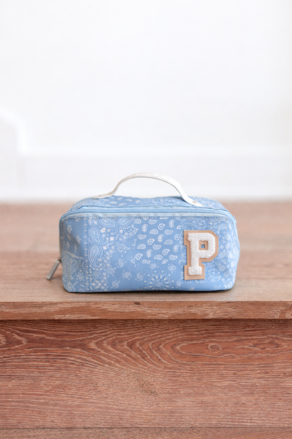 Blue toiletry bag with a 'P' on a wooden surface