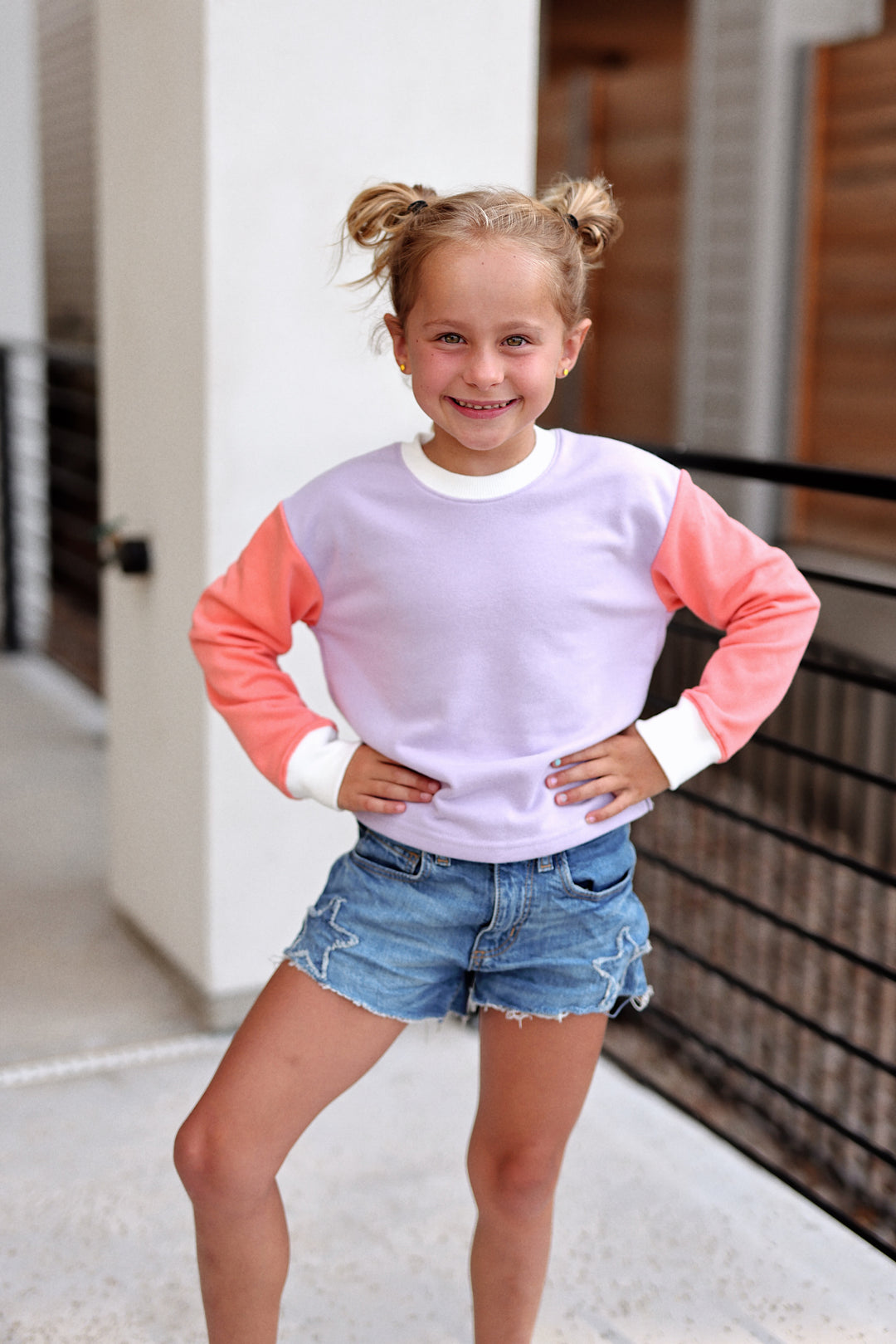 Girls' colorful pullover sweatshirt in lavender and coral with soft fabric, paired with denim shorts.