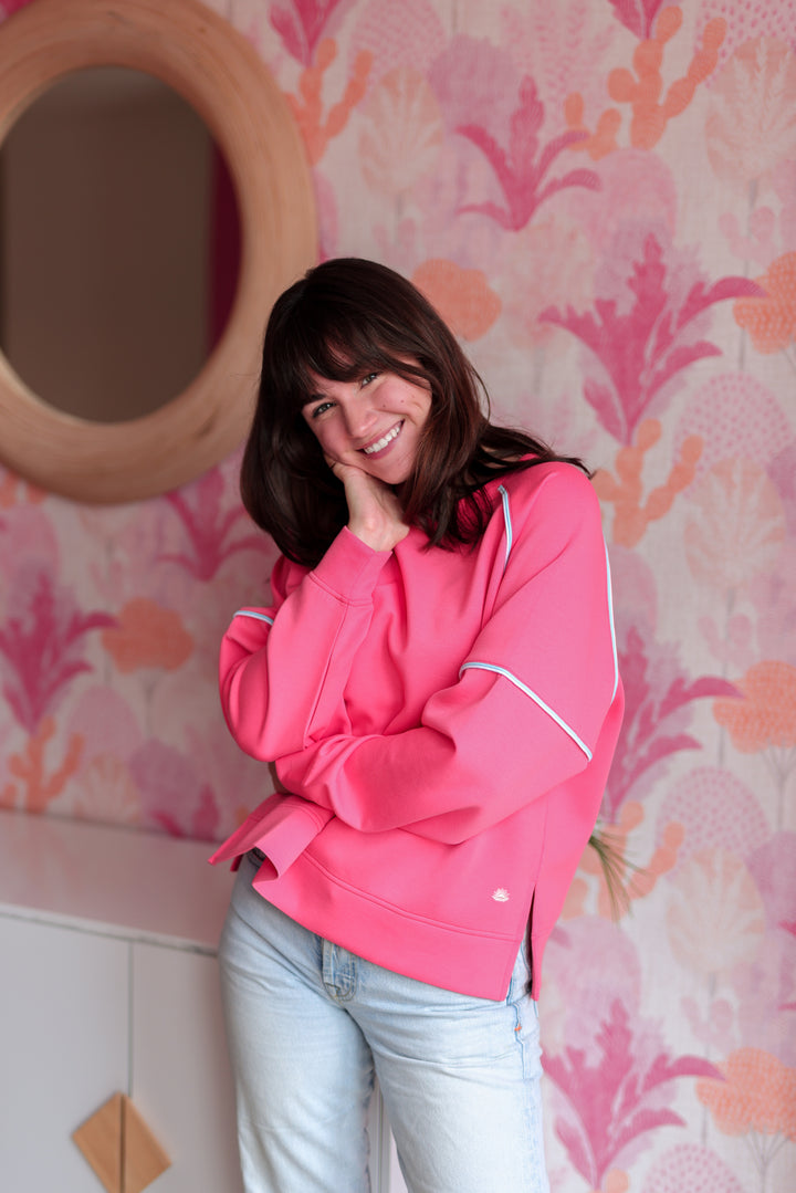 Bright pink women's sweatshirt with stylish design and side slits, paired with light jeans.