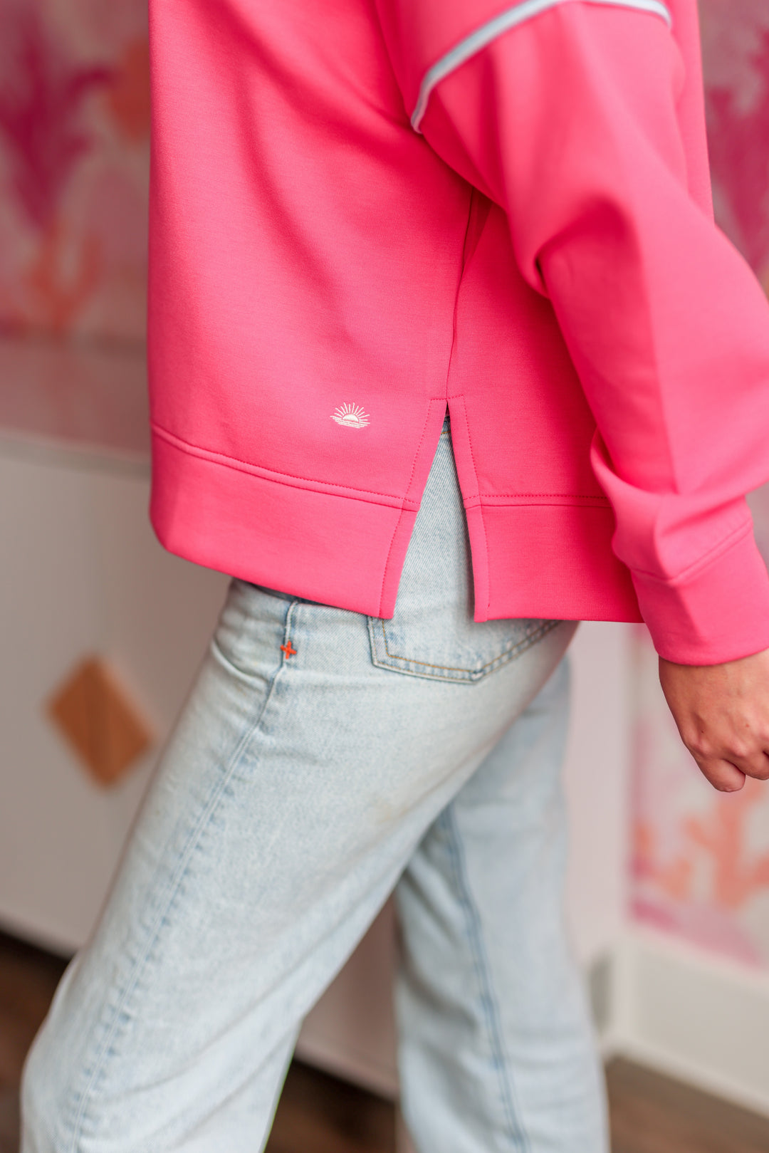 Women's pink sweatshirt with side slits, featuring a relaxed fit and soft fabric, paired with light blue jeans.
