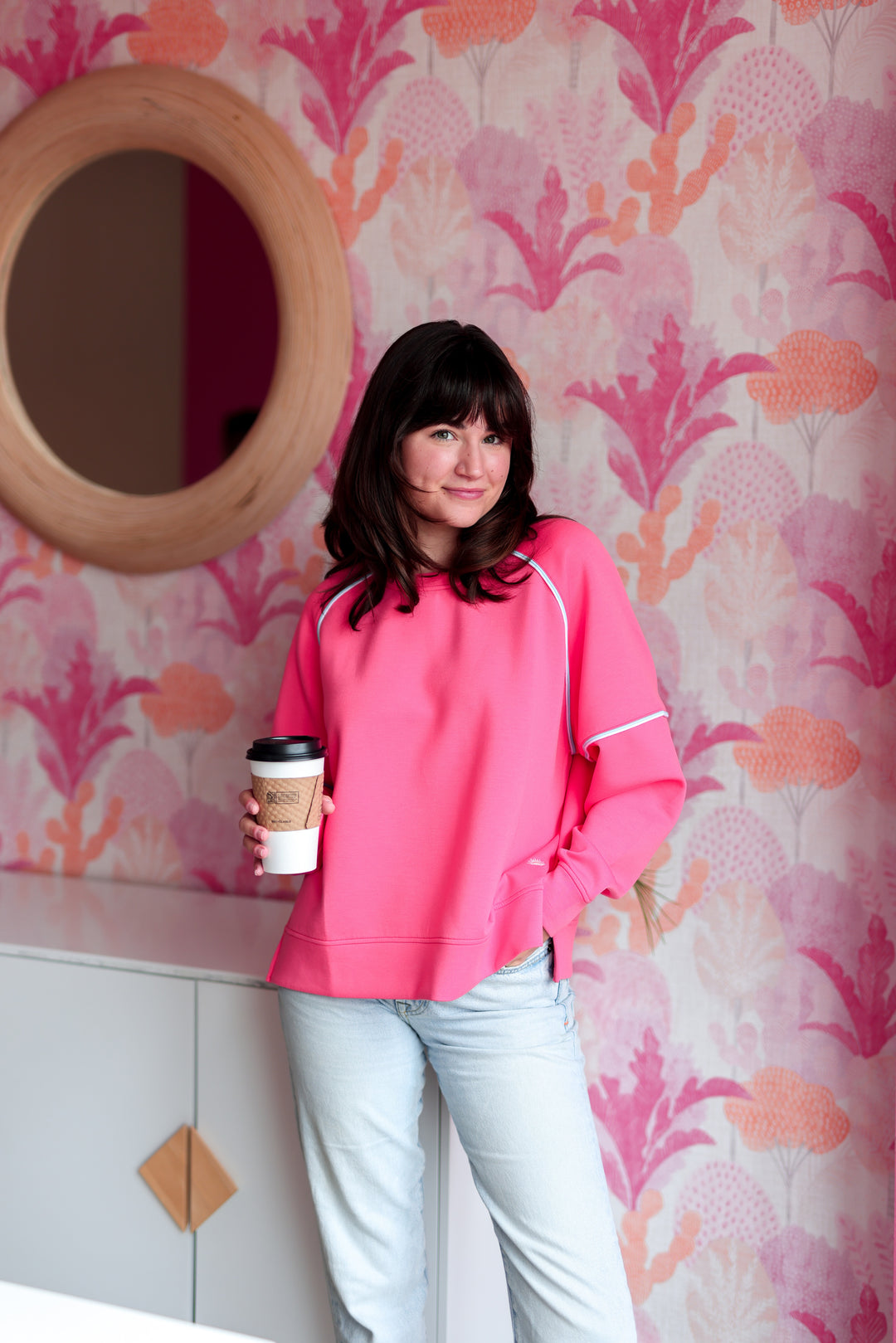 Bright pink women's sweatshirt in soft material, paired with light blue jeans and coffee, stylish and casual look.