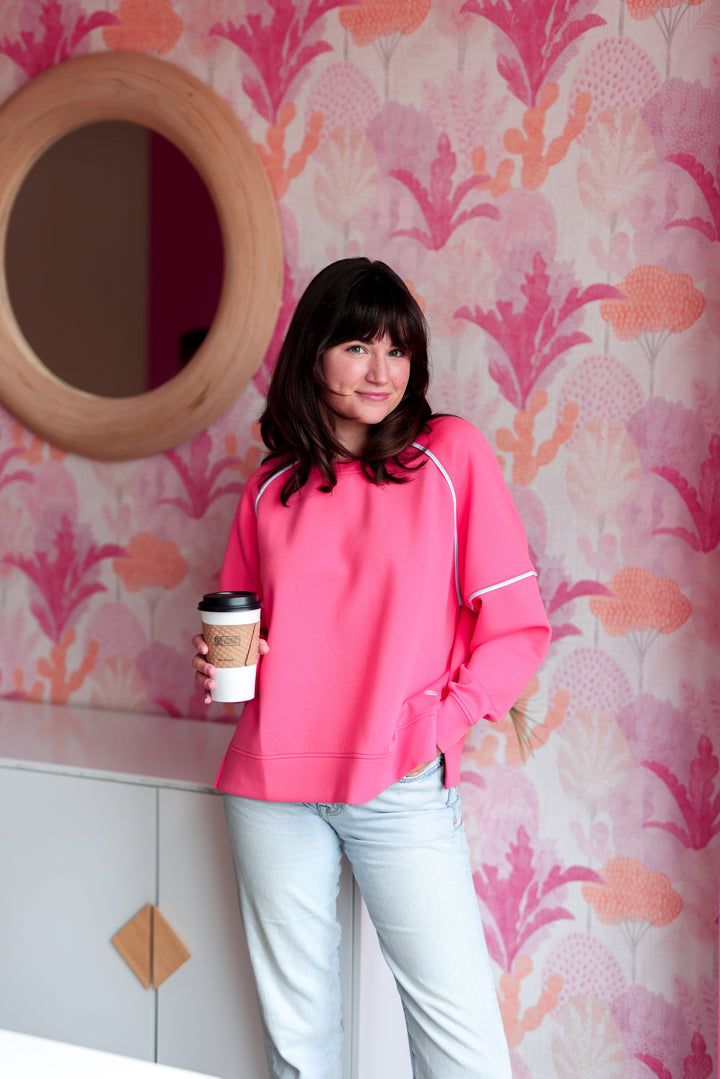 Bright pink women's sweatshirt in soft material, paired with light blue jeans and coffee, stylish and casual look.