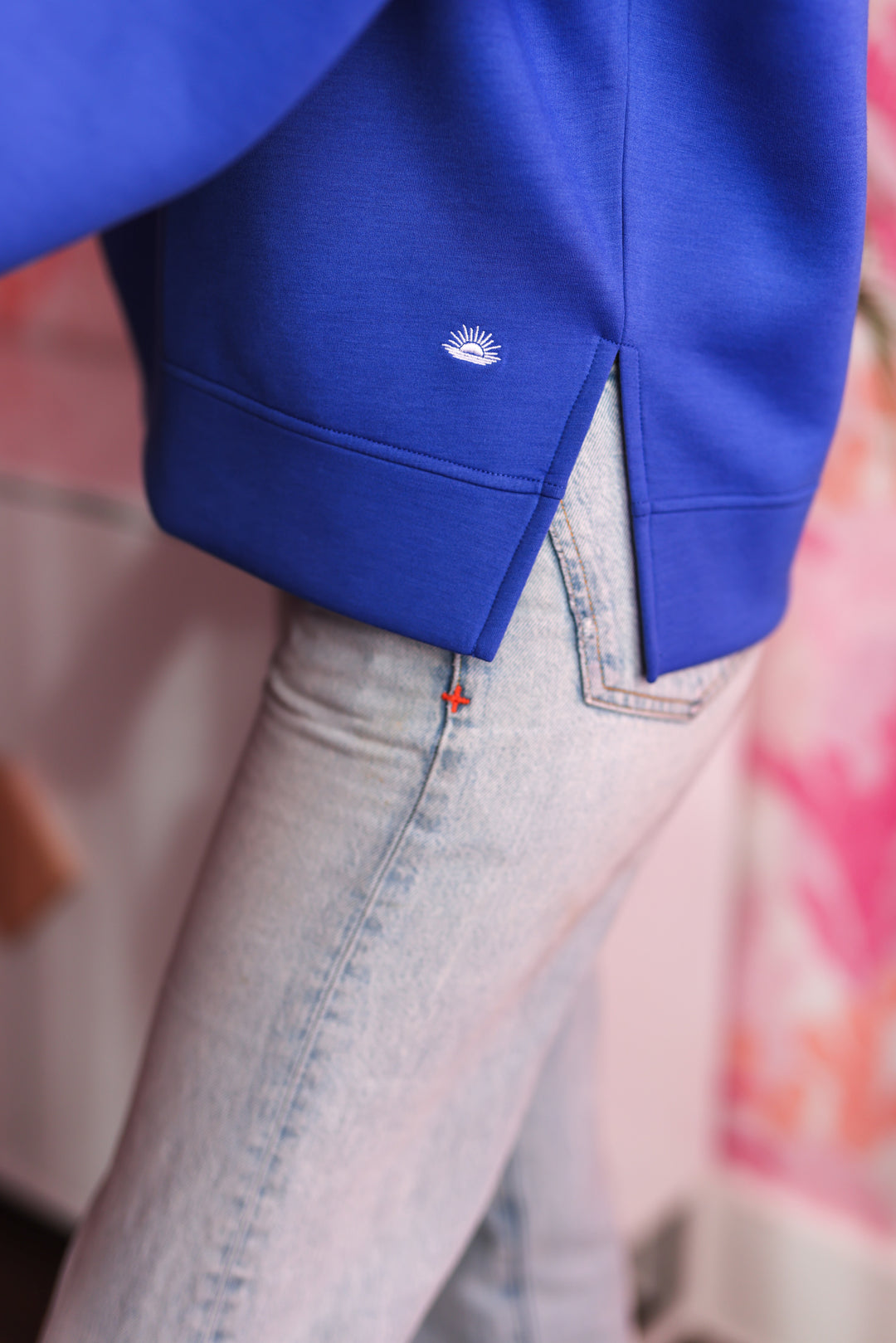 Blue sweatshirt with side slits and embroidered sun logo, paired with light blue jeans.