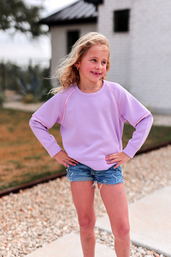 Girl wearing a lavender sweatshirt, relaxed fit, perfect for casual wear, paired with denim shorts.