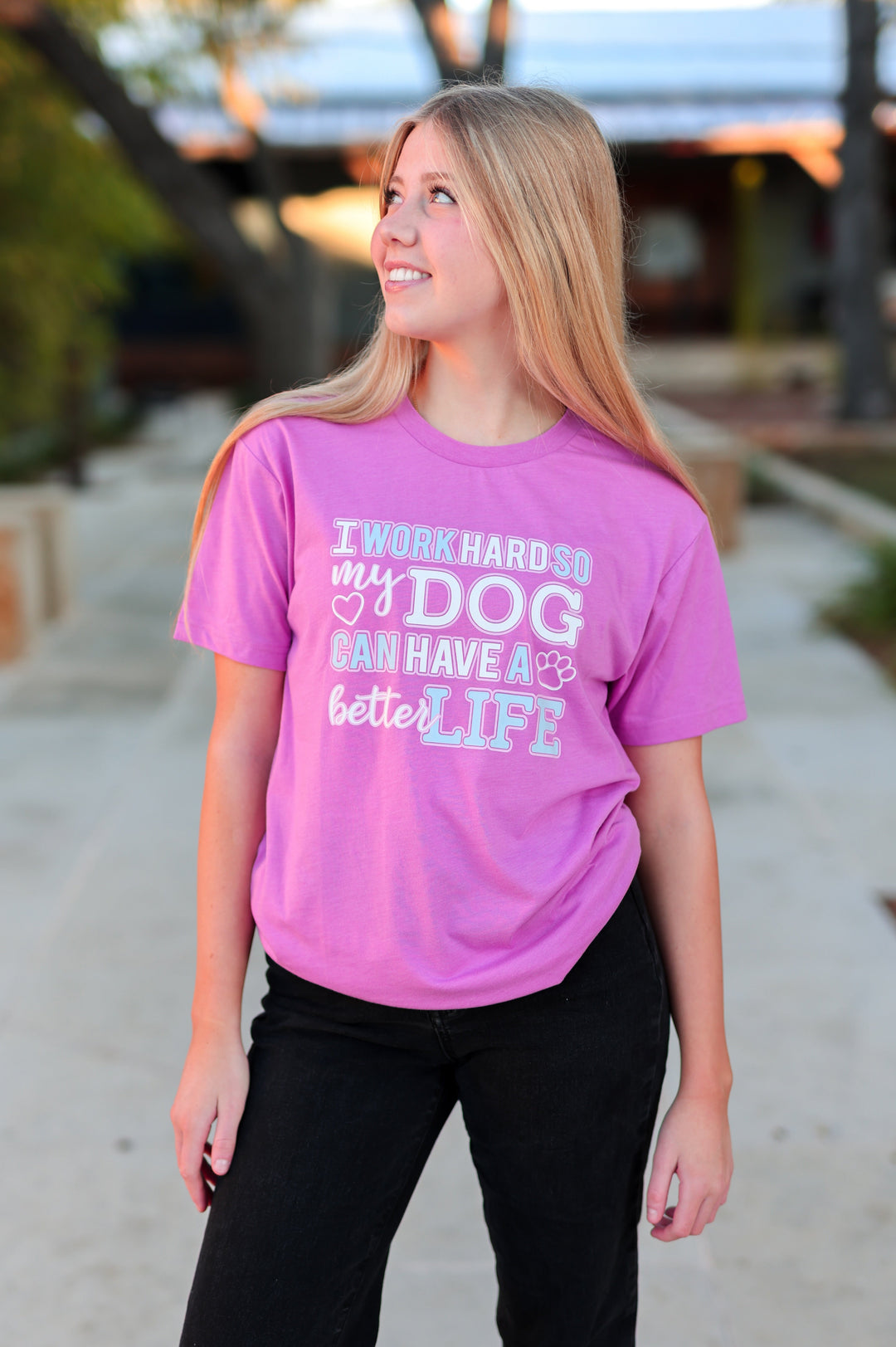 Person wearing a pink t-shirt with a message about a dog, standing outdoors.