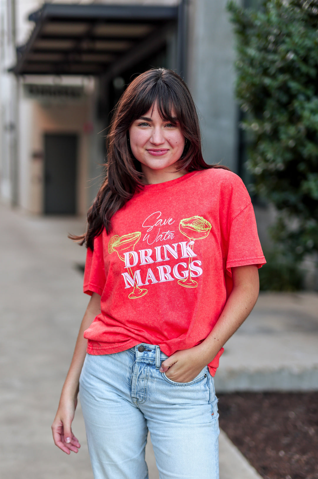 Woman wearing a red t-shirt with text, standing outdoors.