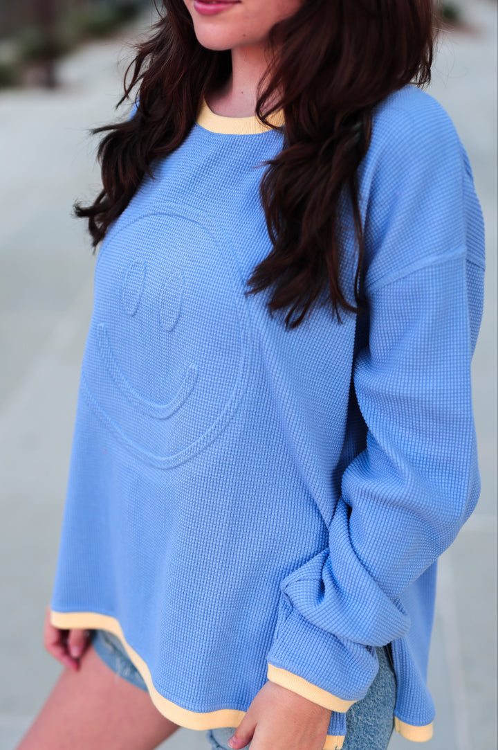 Light blue waffle knit sweatshirt with smiley face design and yellow trim, perfect for casual wear.