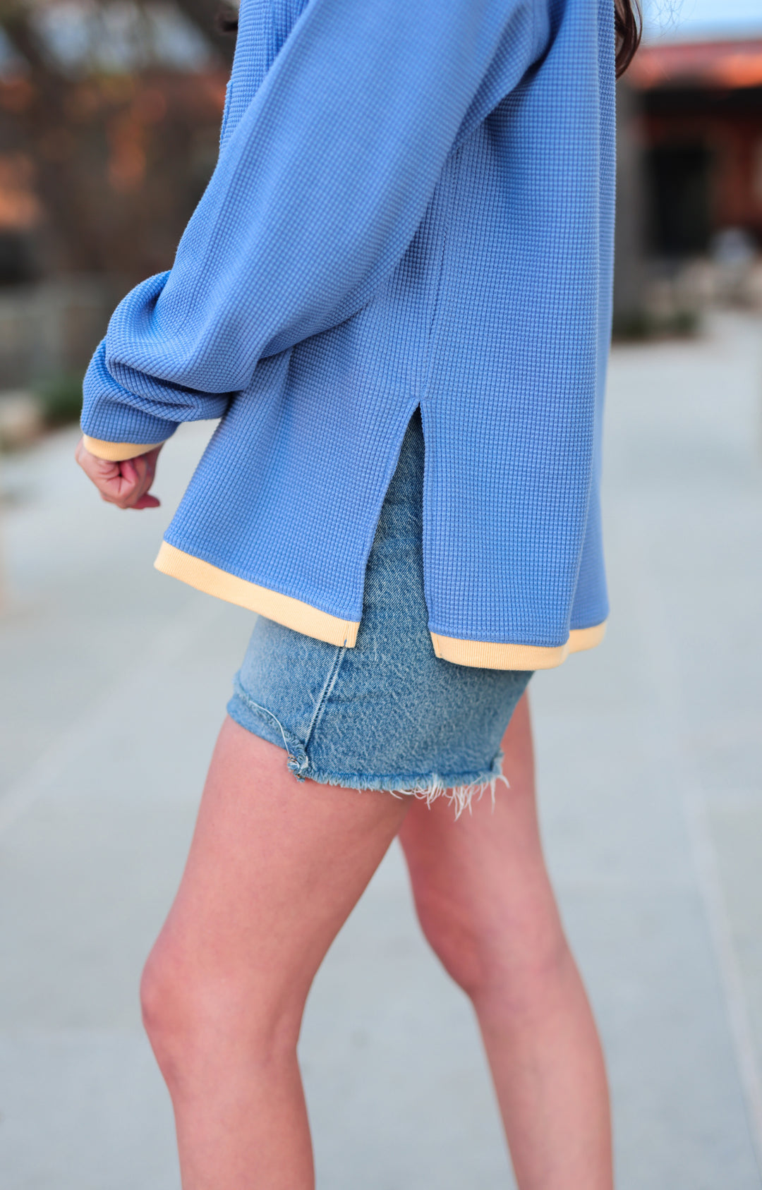 Blue waffle knit oversized sweatshirt with yellow trim, paired with distressed denim shorts.