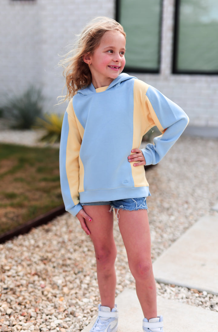 Child wearing a blue and yellow hoodie outdoors on a gravel path.