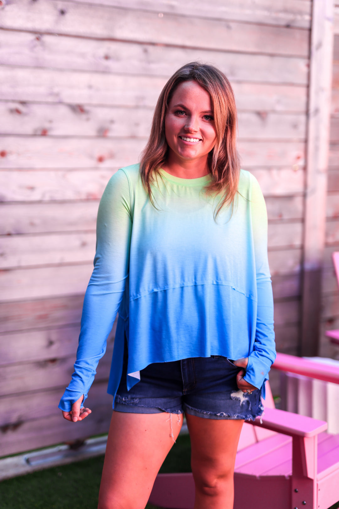 Woman wearing a gradient blue and green long-sleeve top standing outdoors.