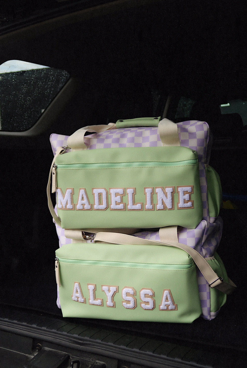 Personalized green and lavender checkered duffel bags with padded handles and front zip pockets.