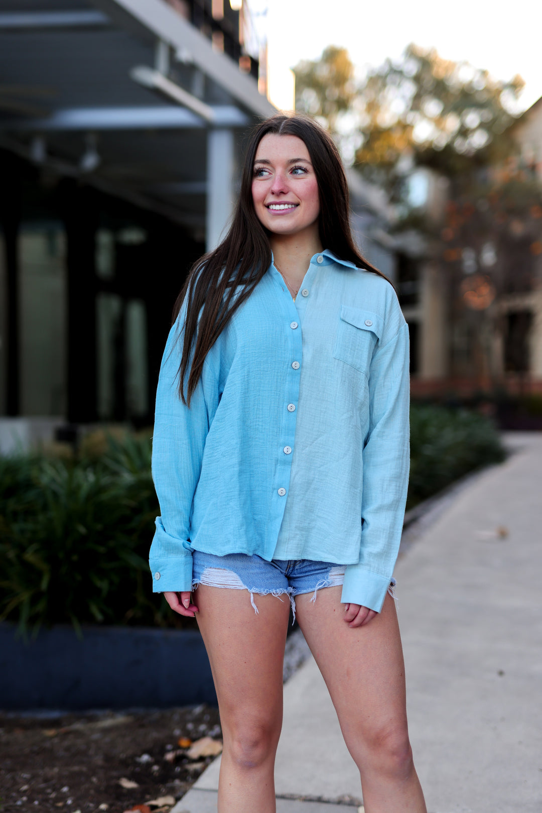 Woman wearing a light blue shirt and denim shorts standing outdoors.
