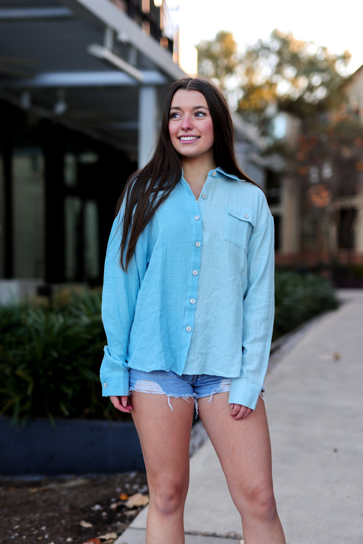 Woman wearing a light blue shirt and denim shorts standing outdoors.