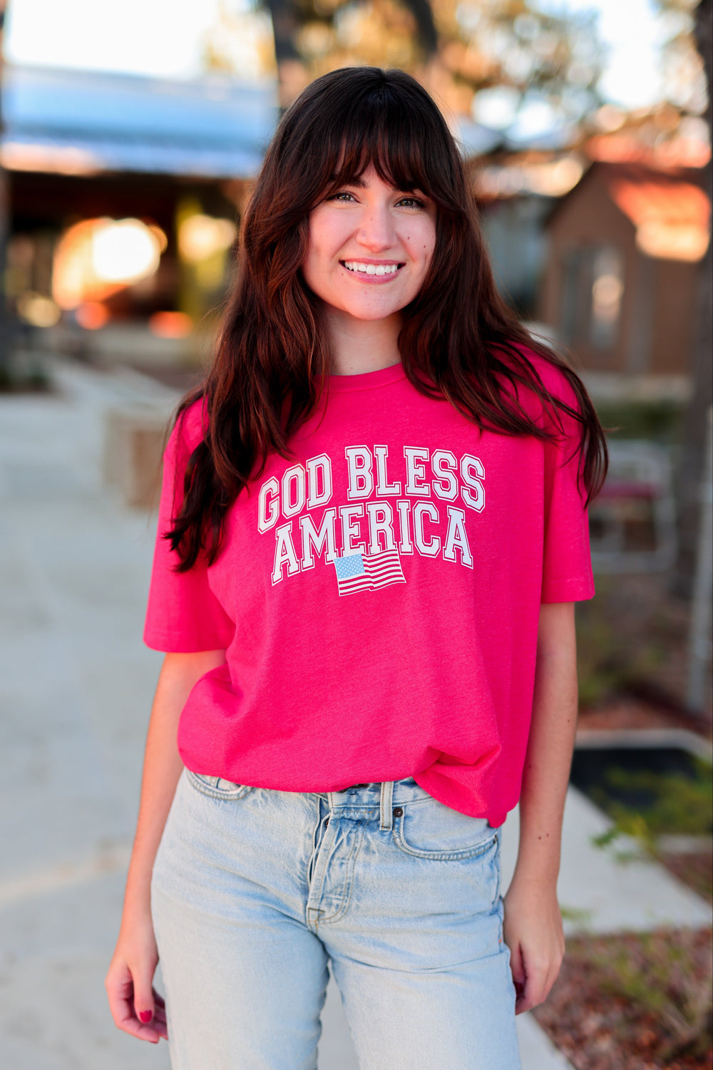 Woman wearing a red 'God Bless America' t-shirt outdoors.