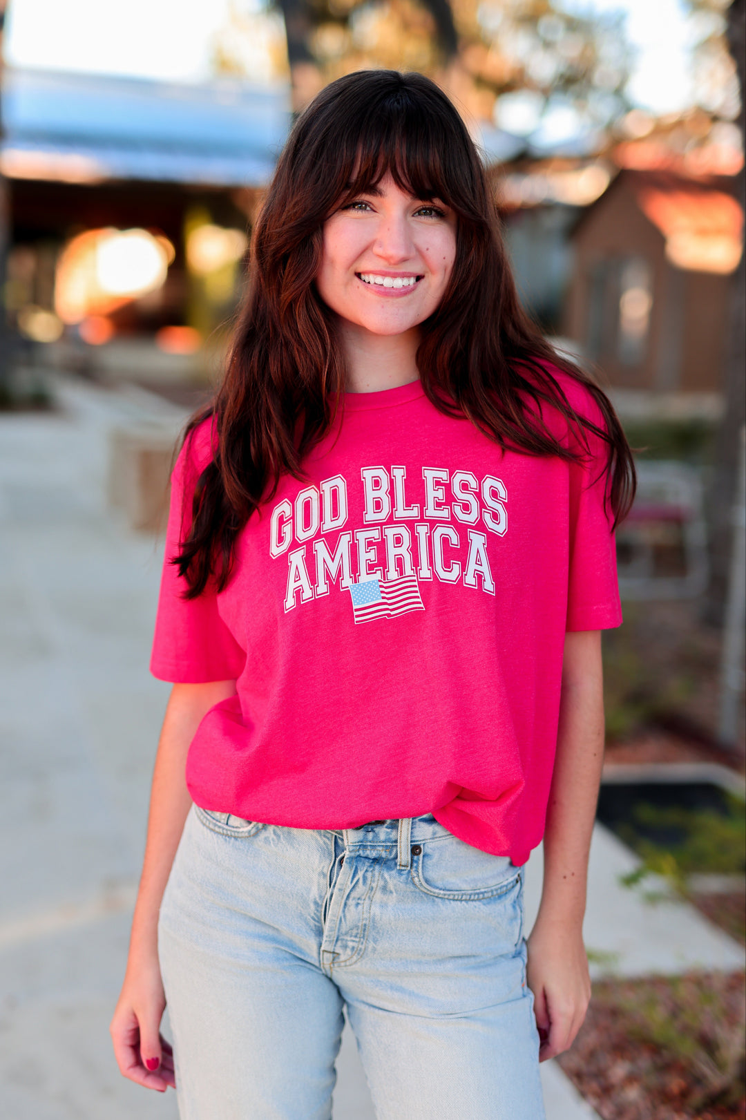 Woman wearing a red 'God Bless America' t-shirt outdoors.