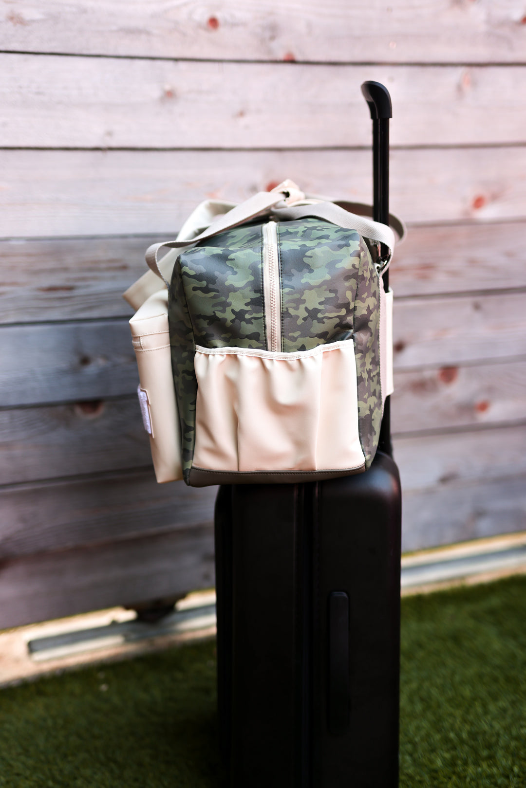 Camouflage travel bag in green and cream, featuring a zipper and side pockets, resting on a suitcase.