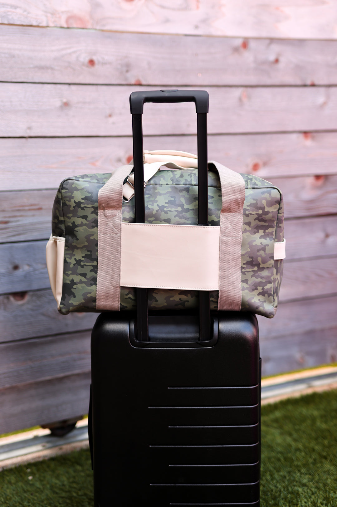 Camouflage duffel bag with beige straps, placed on a black suitcase, perfect for travel and adventure.