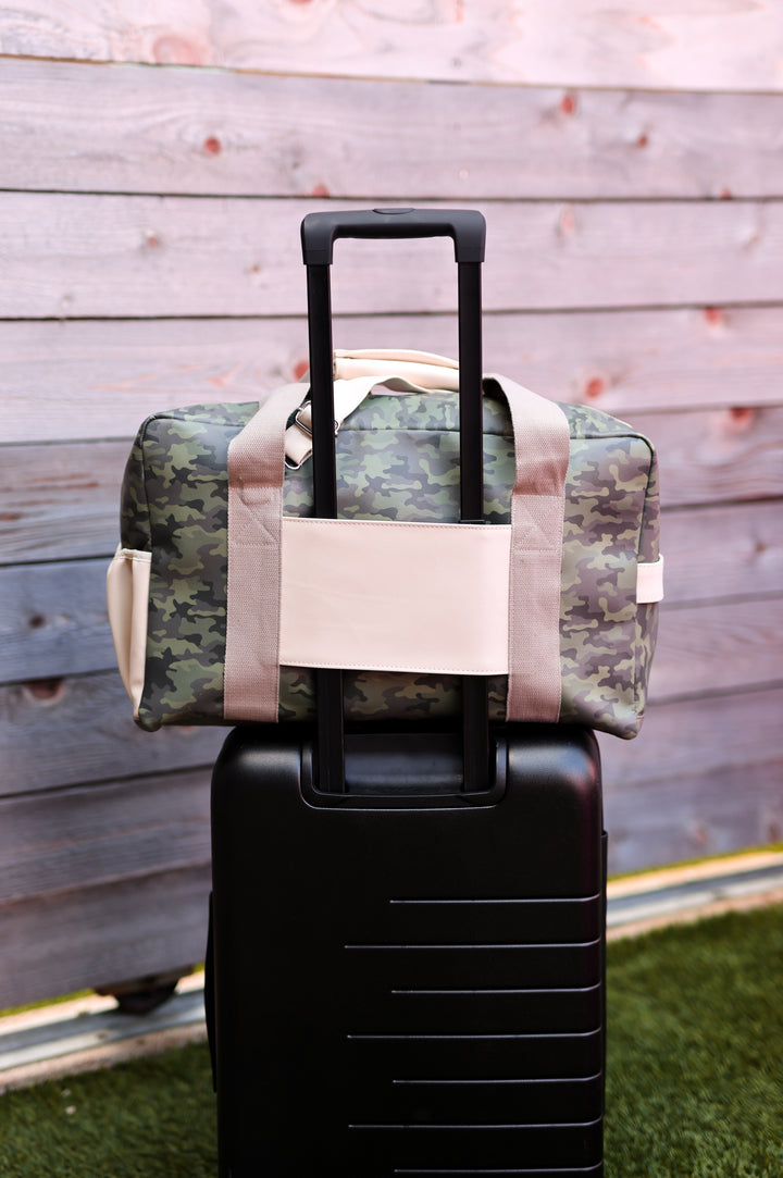 Camouflage duffel bag with beige straps, placed on a black suitcase, perfect for travel and adventure.