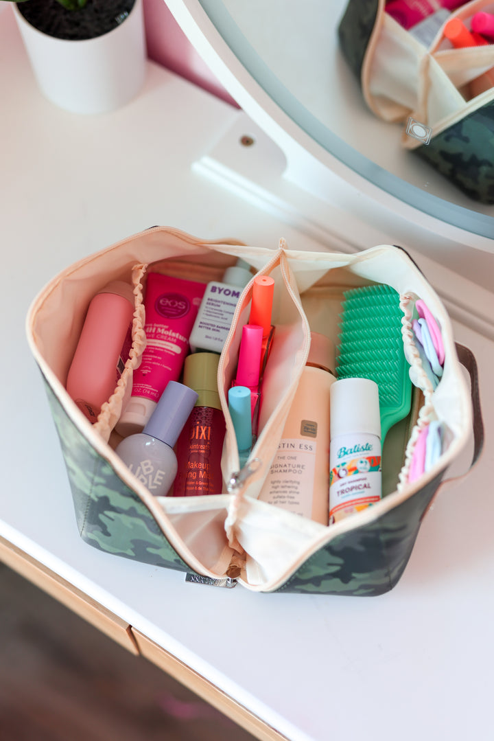 Camo cosmetic bag with skincare and hair products, featuring divided compartments for organization.