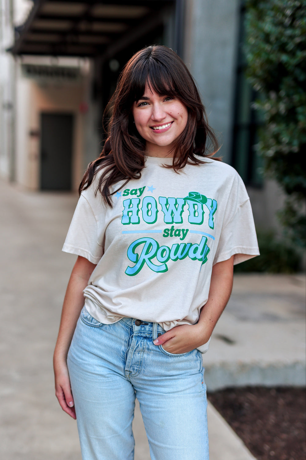 Woman wearing a t-shirt with 'Say Howdy, Stay Rowdy' text outdoors.