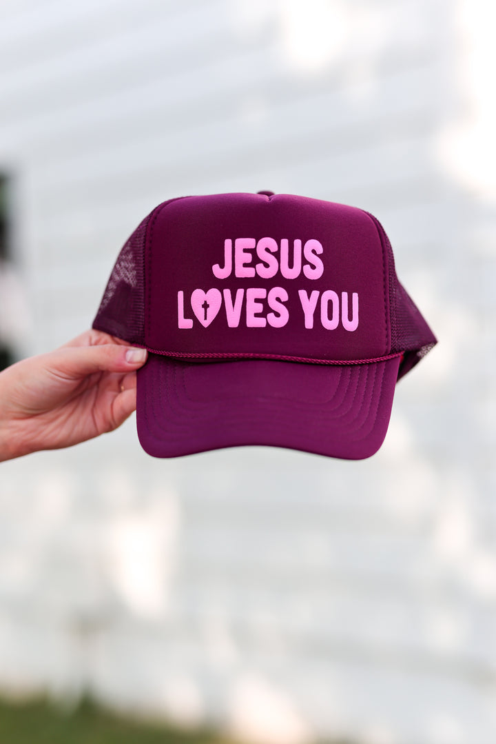Maroon trucker hat with 'Jesus Loves You' graphic in pink, ideal for casual wear or religious events.