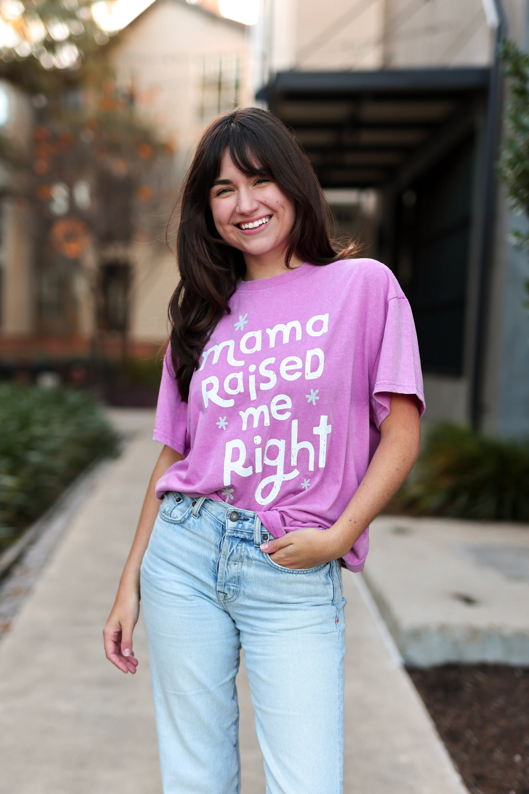 Woman wearing a pink t-shirt with text, standing outdoors.
