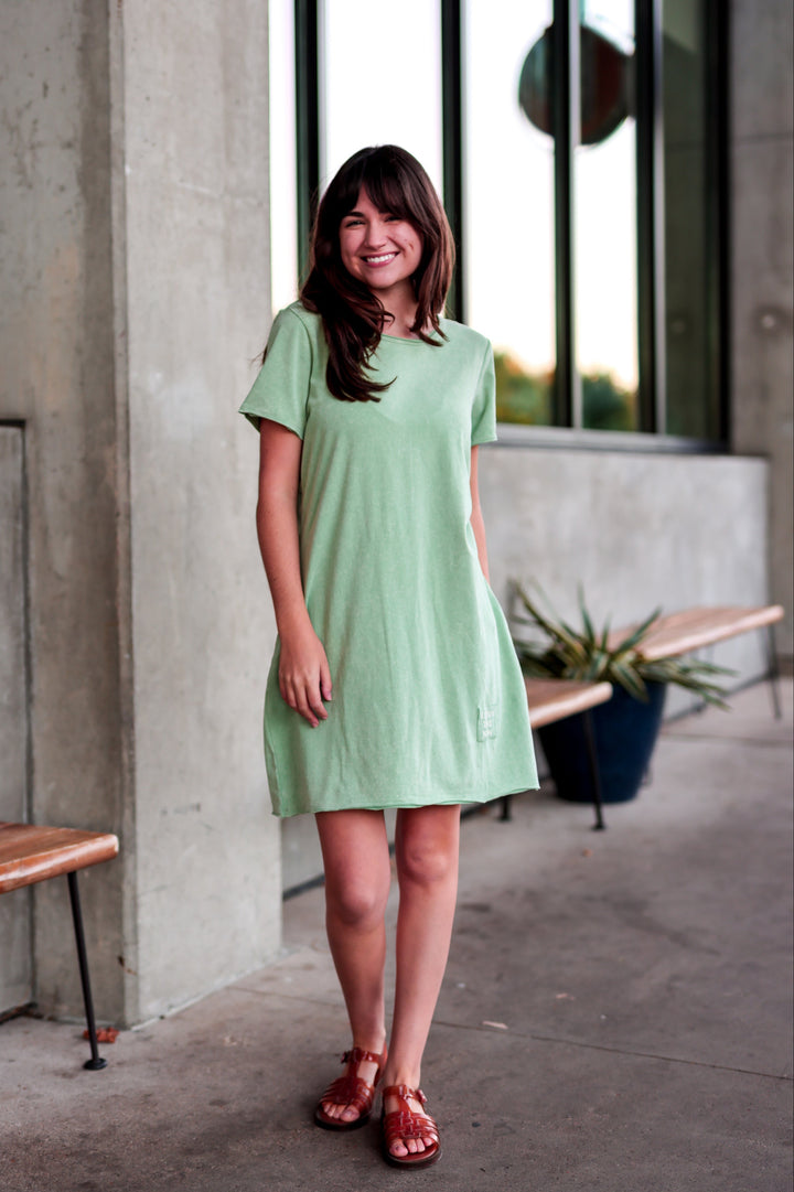 Woman in a light green dress standing in front of a building with large windows.