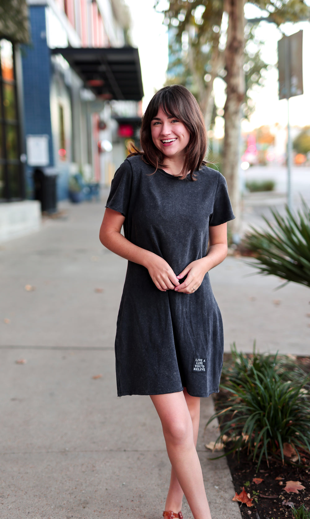 Woman wearing a dark gray dress with a logo on a city street.