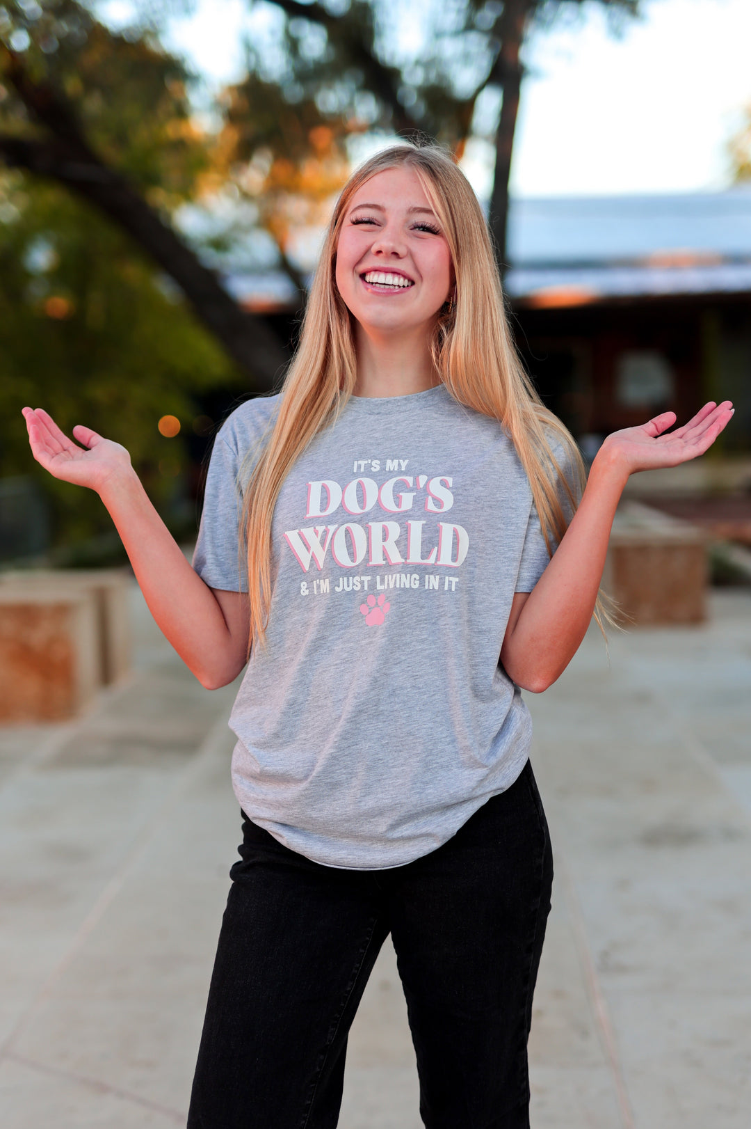 Person wearing a gray t-shirt with text, standing outdoors with arms outstretched.