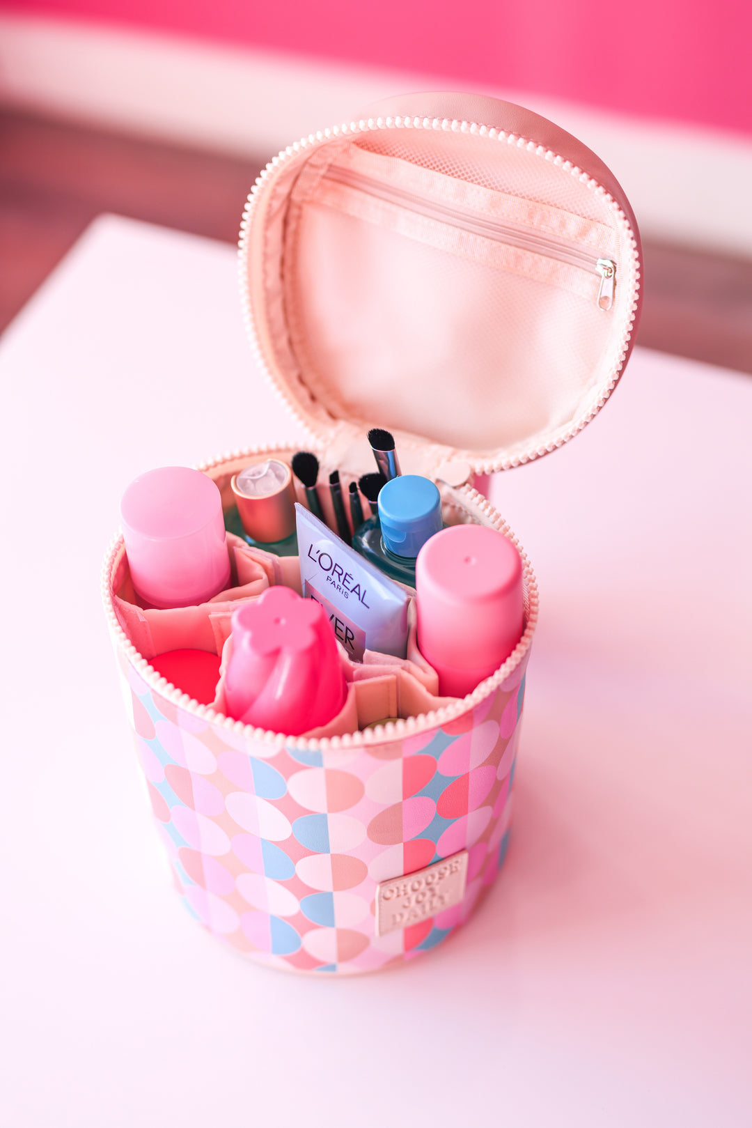 Pink round cosmetic bag with various beauty products, including bottles and brushes, organized neatly inside.