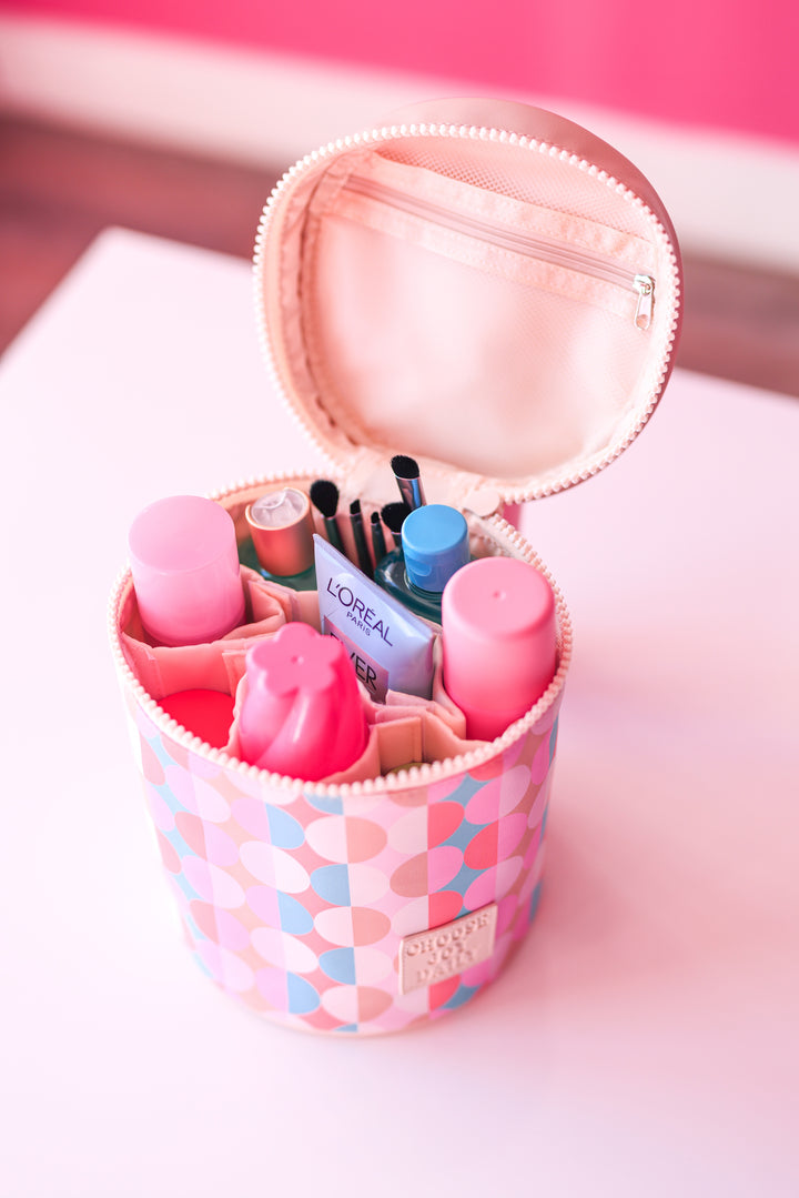 Pink round cosmetic bag with various beauty products, including bottles and brushes, organized neatly inside.