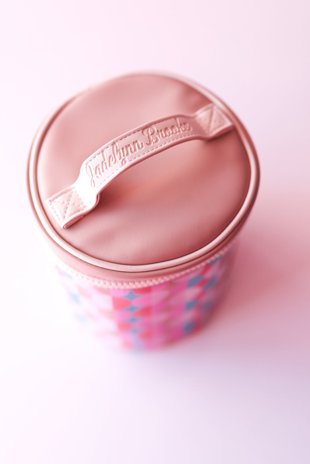 Round pink storage container with a lid and handle featuring colorful geometric patterns.