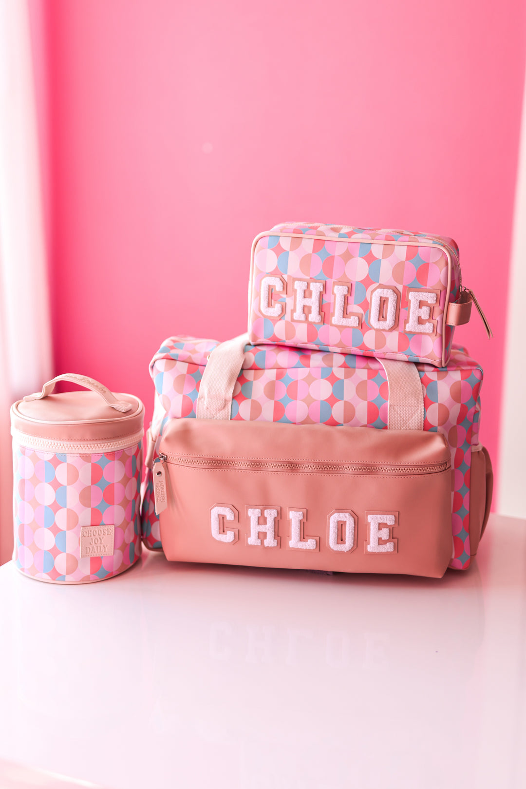 Colorful Chloe travel bag set including a duffel, toiletry bag, and container in pink and geometric patterns.