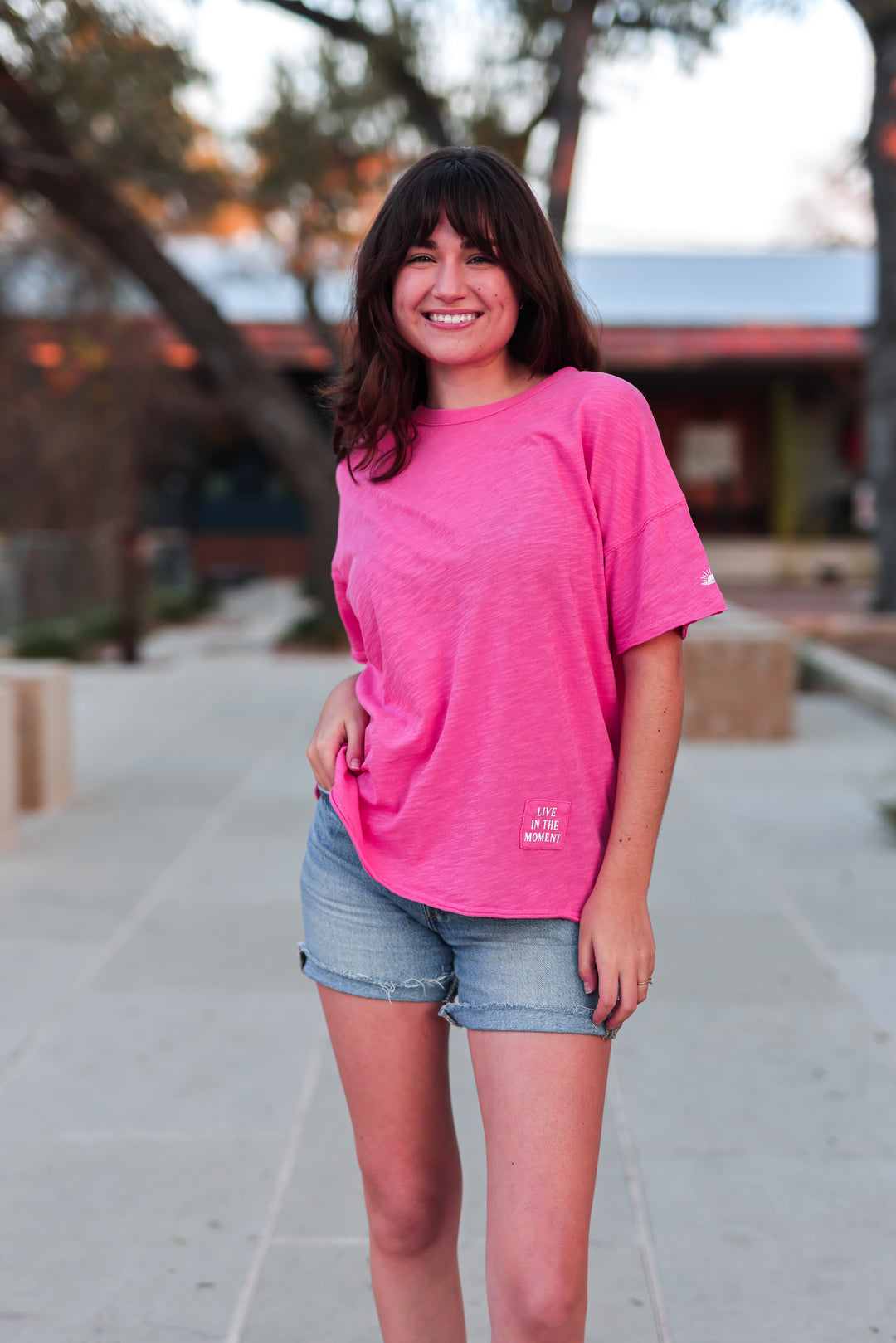 Person wearing a pink t-shirt and denim shorts standing outdoors.