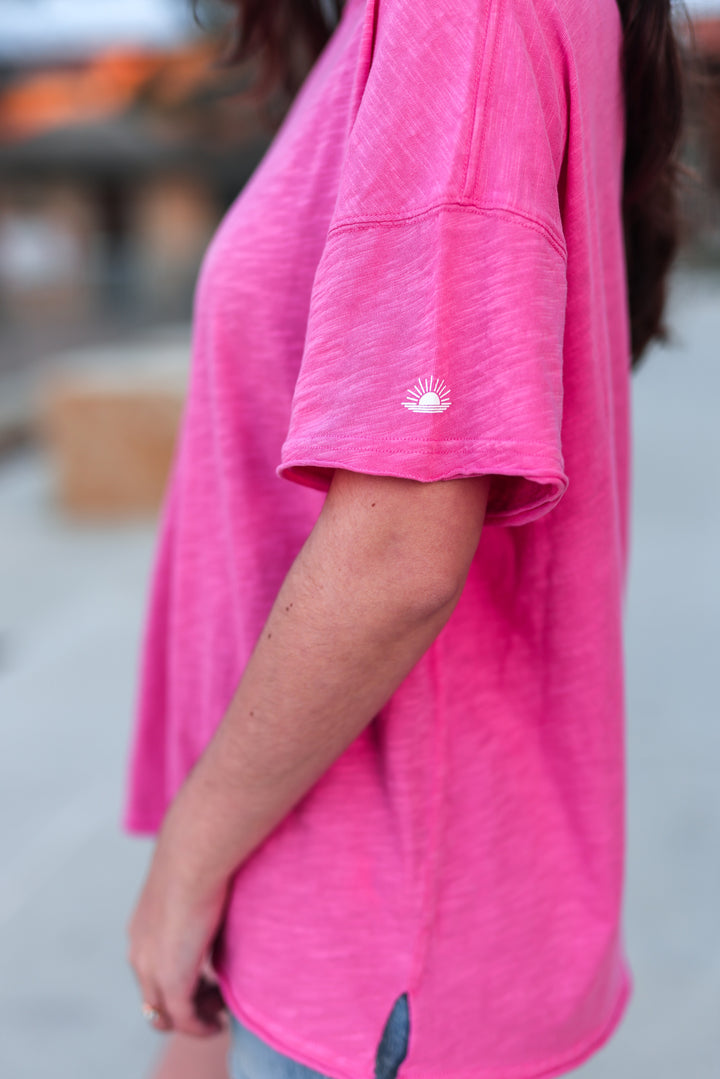 Women's casual pink t-shirt made of soft fabric, featuring a sun logo on the sleeve and relaxed fit.