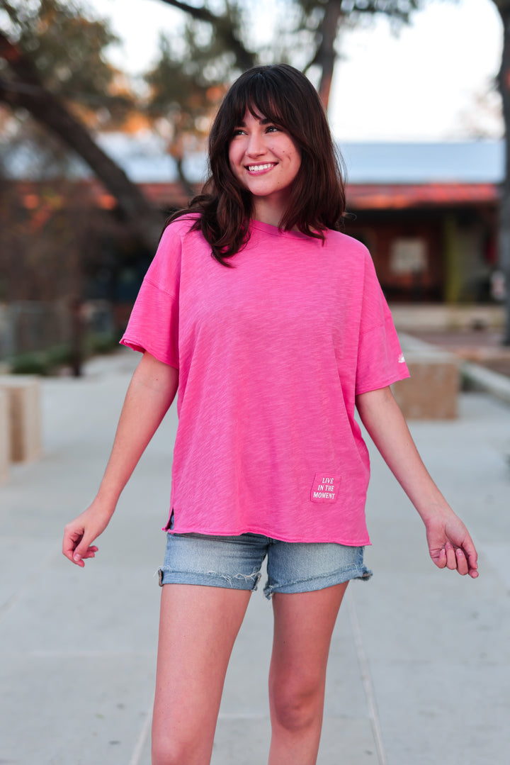 Women's pink oversized t-shirt made of soft fabric featuring 'Live in the Moment' graphic.