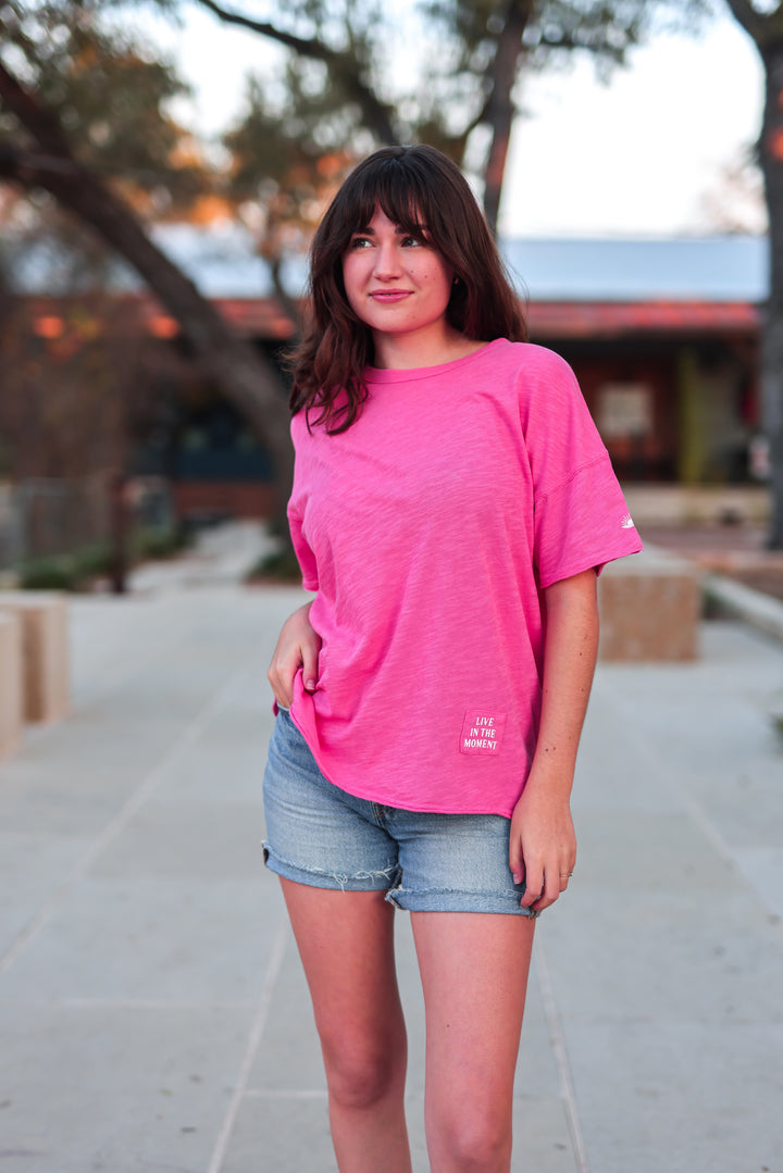 Person wearing a bright pink t-shirt and denim shorts standing outdoors.