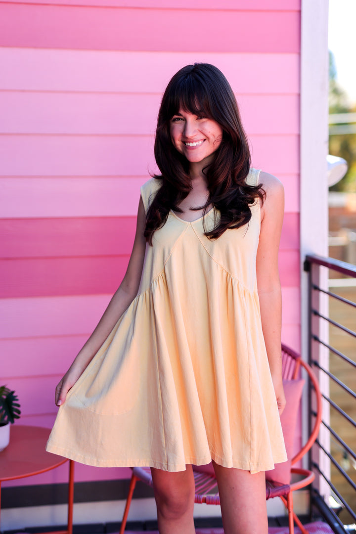 Woman in a yellow dress standing in front of a pink wall