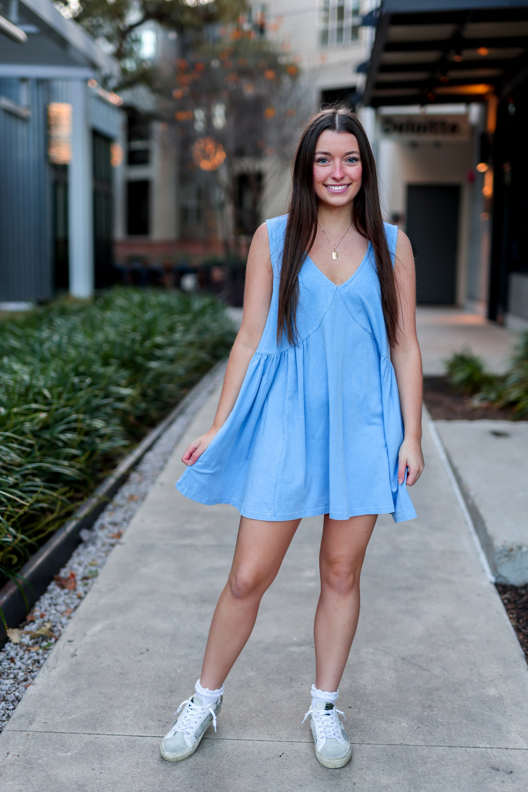 Woman in a light blue dress standing on a sidewalk with buildings in the background