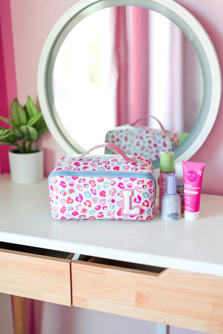 Pink leopard print makeup bag on a vanity with mirror and skincare products.