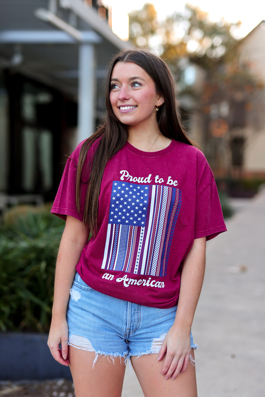 Woman wearing a purple t-shirt with an American flag design and text, standing outdoors.