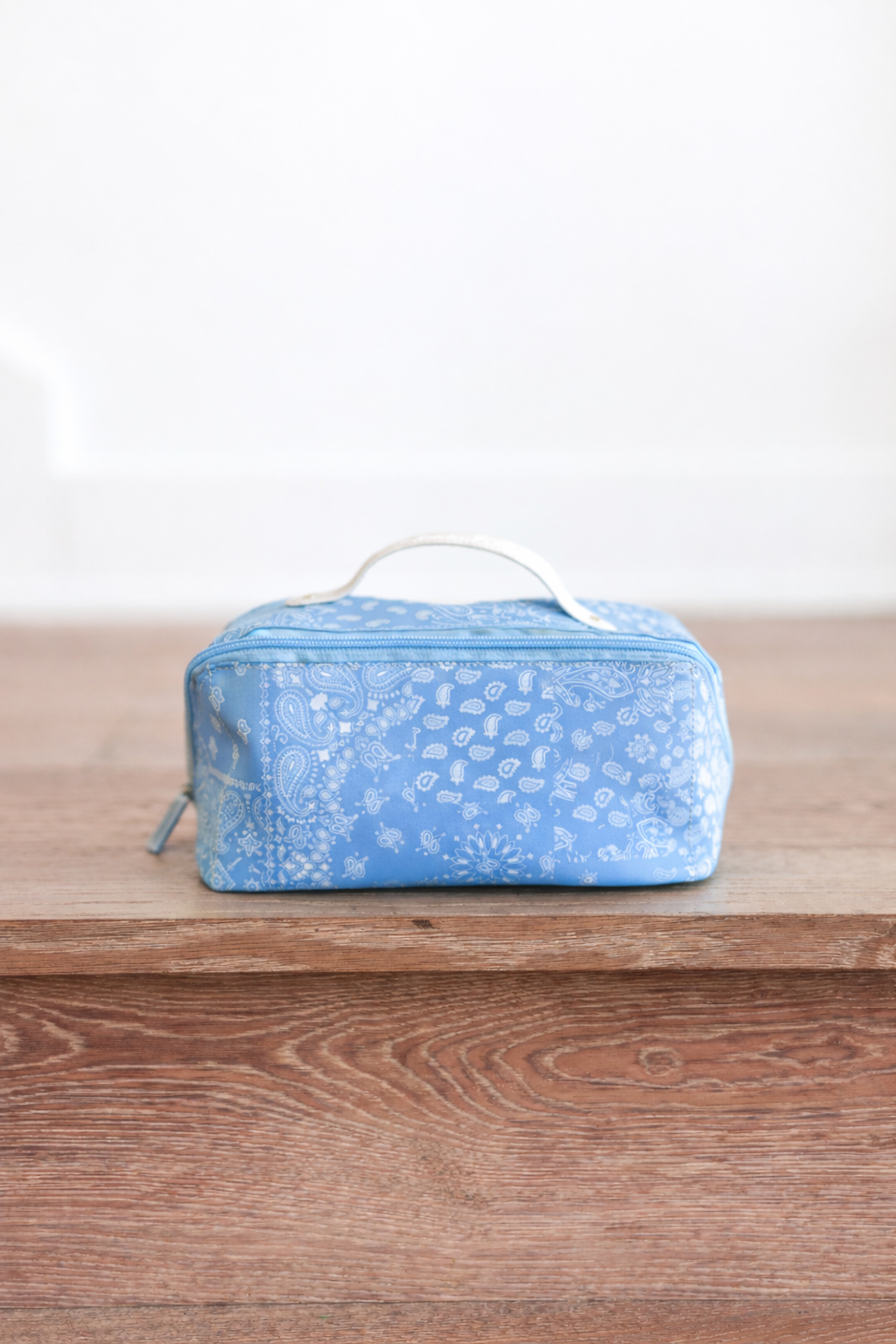 Blue toiletry bag with paisley pattern on a wooden surface