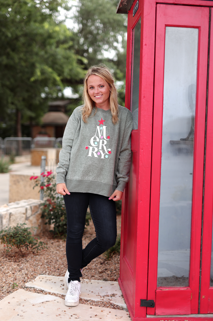 Women's green sweatshirt with 'Merry' graphic, paired with dark jeans and white sneakers.